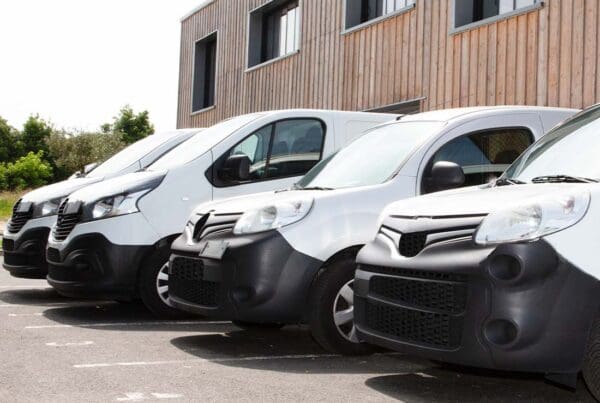 Fleet Insurance - Delivery Service of White Vans and Small Trucks Parked in a Row in Front of Factory Warehouse Distribution Plant on a Sunny Day