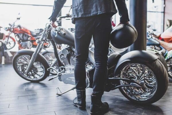 Motorcycle Dealership Insurance - View of Man From Behind Holding a Motorcycle Helmet and Looking at a Motorcycle in a Dealership Shop